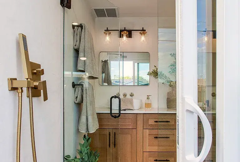 Brass shower fixture in the foreground, oak vanity beyond, shot through the shower glass.