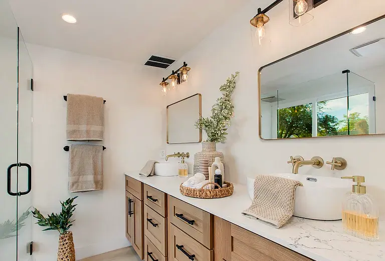 Primary bath: double vessel sinks, wall mounted brass faucets, oak vanity, brass framed mirrors.