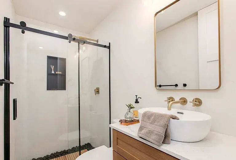 Second bath: teak shower floor over river rock, vessel sink, brass framed mirror.