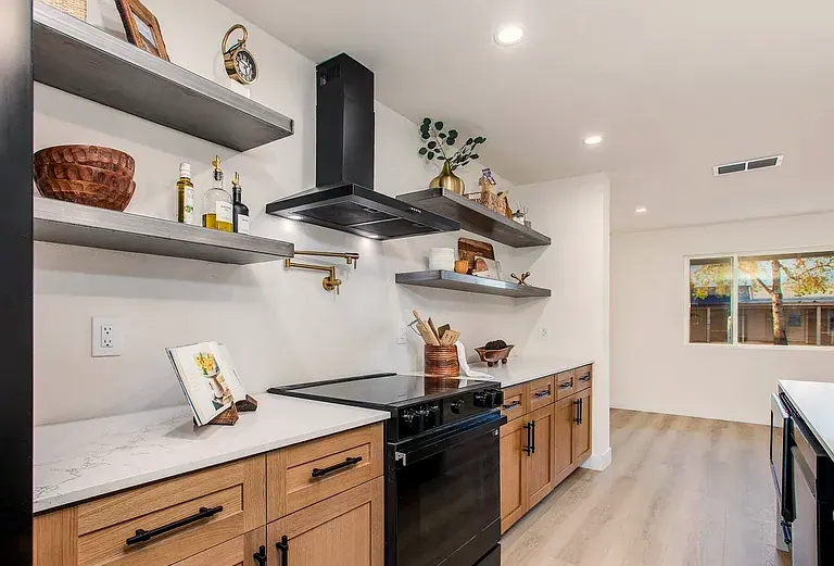 Kitchen detail: brass pot filler over a black range, floating shelves, oak cabinetry.