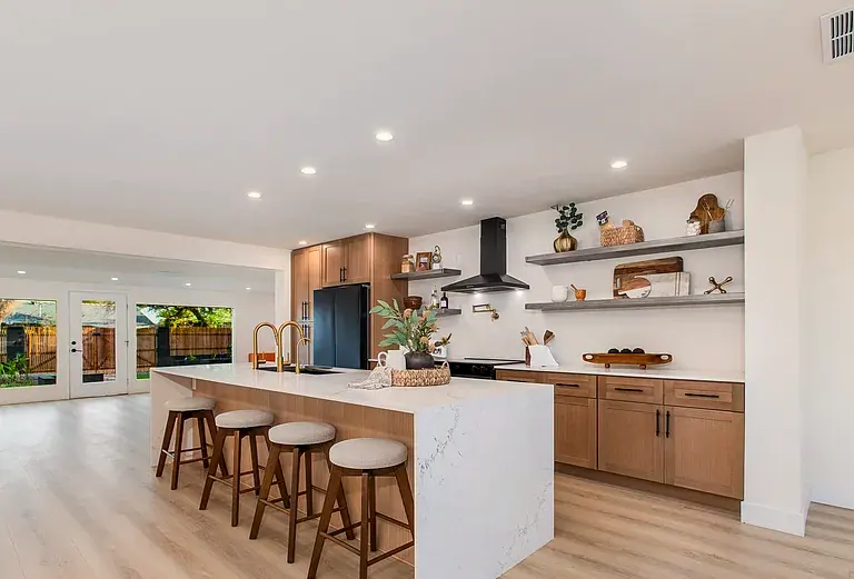 Waterfall quartz island with four stools, white oak cabinetry, black hood, open to the living space.
